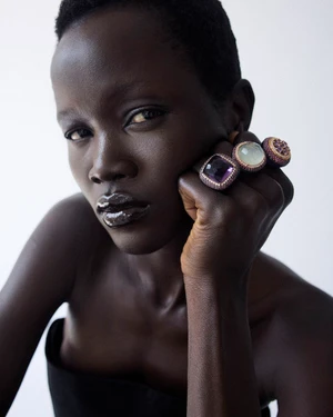 Model Anyiel Majok rests her hand on her chin showcasing large gemstone statement rings against a white backdrop.