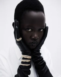 Model Anyiel Majok wearing black leather gloves and gold rings against a white background for Amica project Oro Puro.