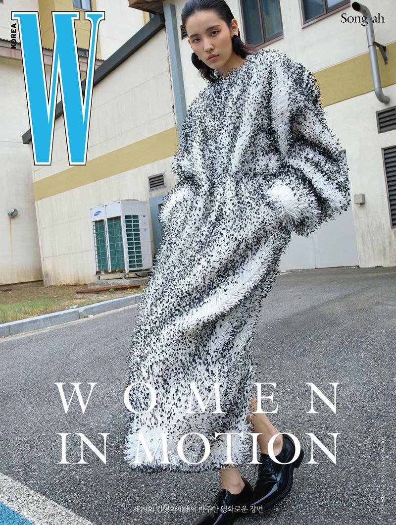 Model Song Ah Woo wearing a voluminous textured black and white coat while posing on an asphalt driveway near a building.