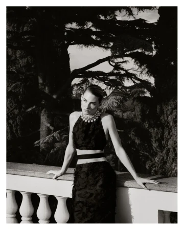 Grace Elizabeth leaning against a stone balustrade wearing a black textured two-piece outfit and statement pearl necklace in monochrome.