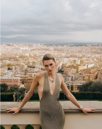 Grace Elizabeth poses on a stone balustrade overlooking a panoramic cityscape in a plunging metallic knit dress and snake necklace.