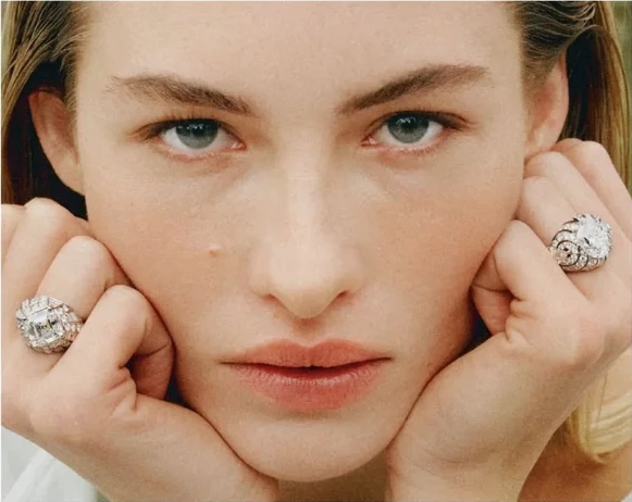 Close-up beauty portrait of model Grace Elizabeth resting her chin on her hands while wearing large diamond cocktail rings.