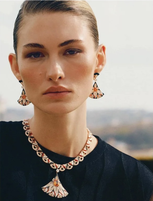 Model Grace Elizabeth wearing fan-shaped gemstone earrings and a matching necklace with a black top against a blurred background.