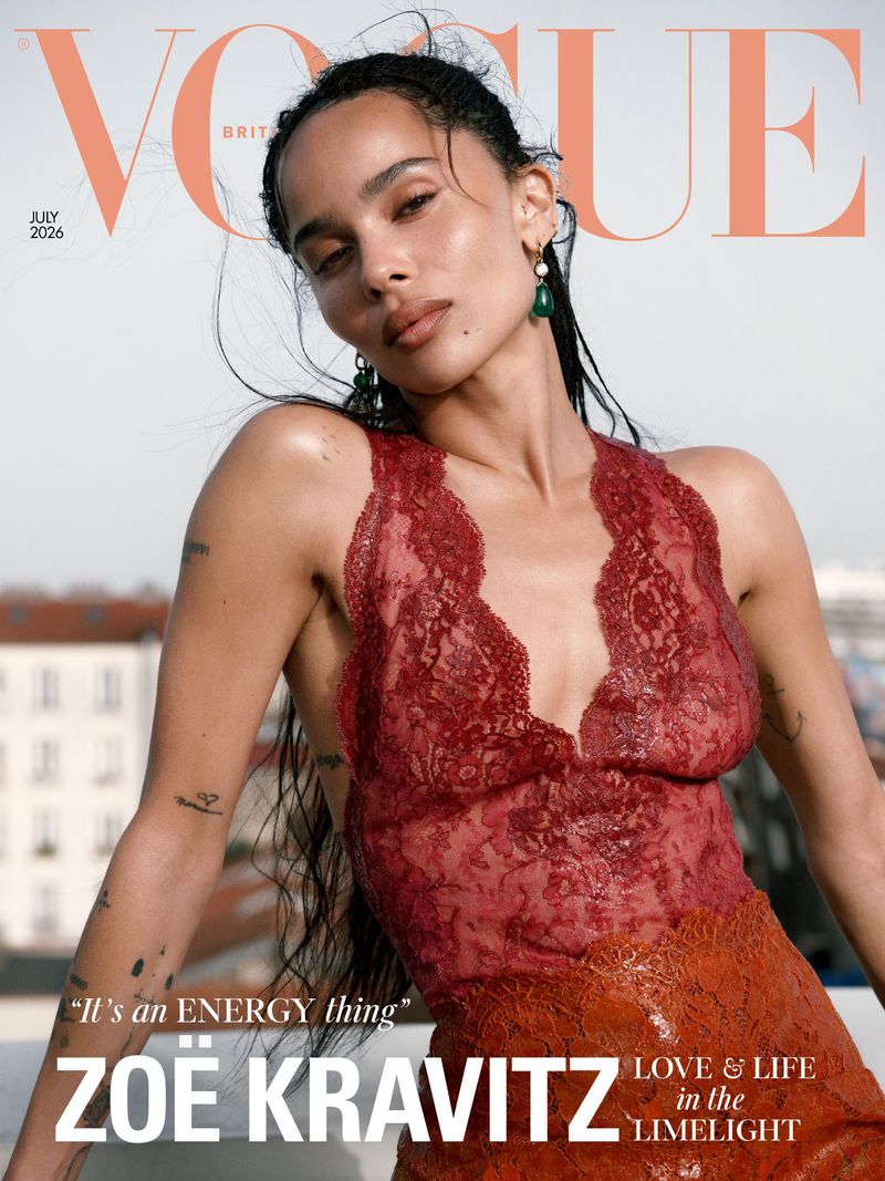 Zoë Kravitz posing outdoors on a rooftop wearing a red sheer lace halter top and green teardrop earrings for British Vogue.