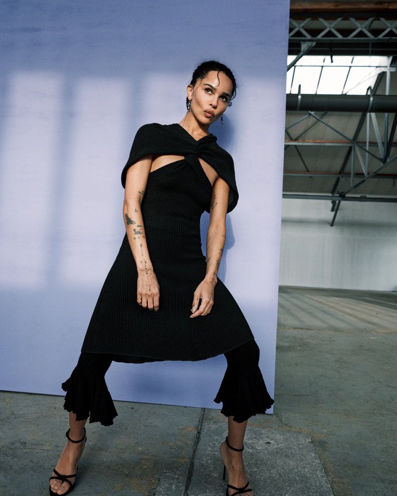 Zoë Kravitz posing in a black cut-out knit dress and strappy heels against a lavender backdrop for British Vogue.