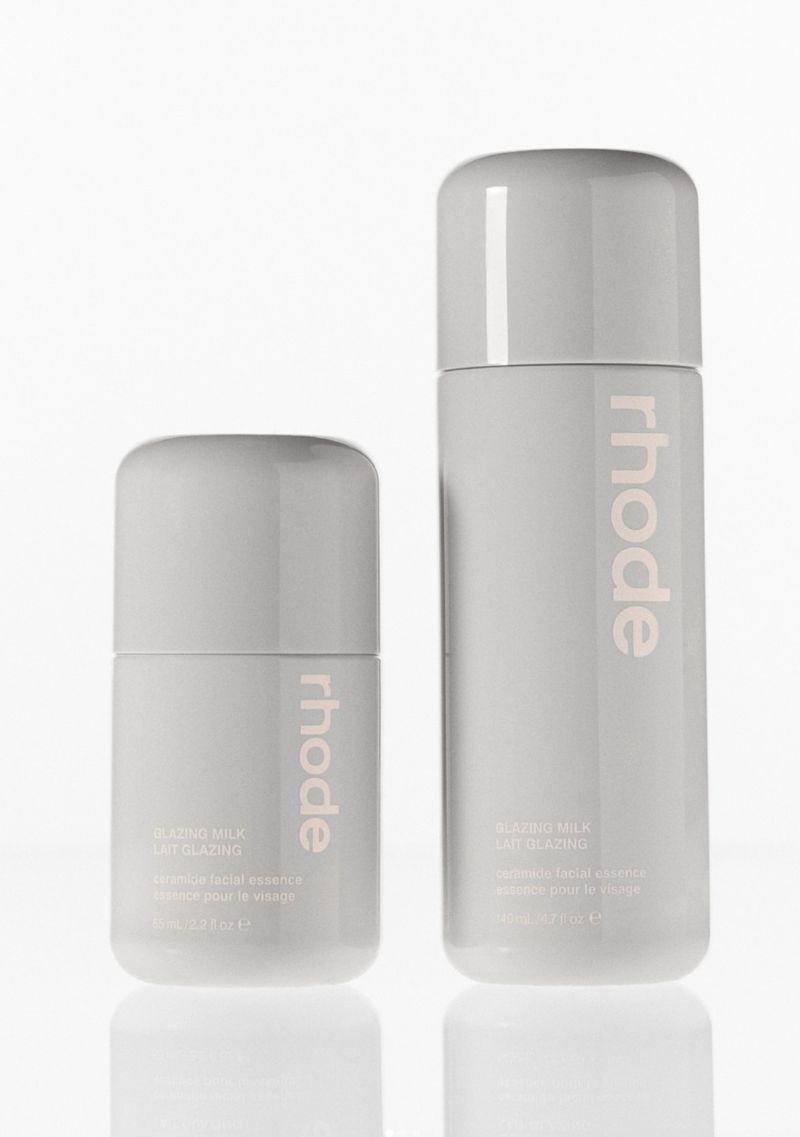 Two grey Rhode skincare bottles are positioned against a stark white background, featuring light pink logos and minimal product information.