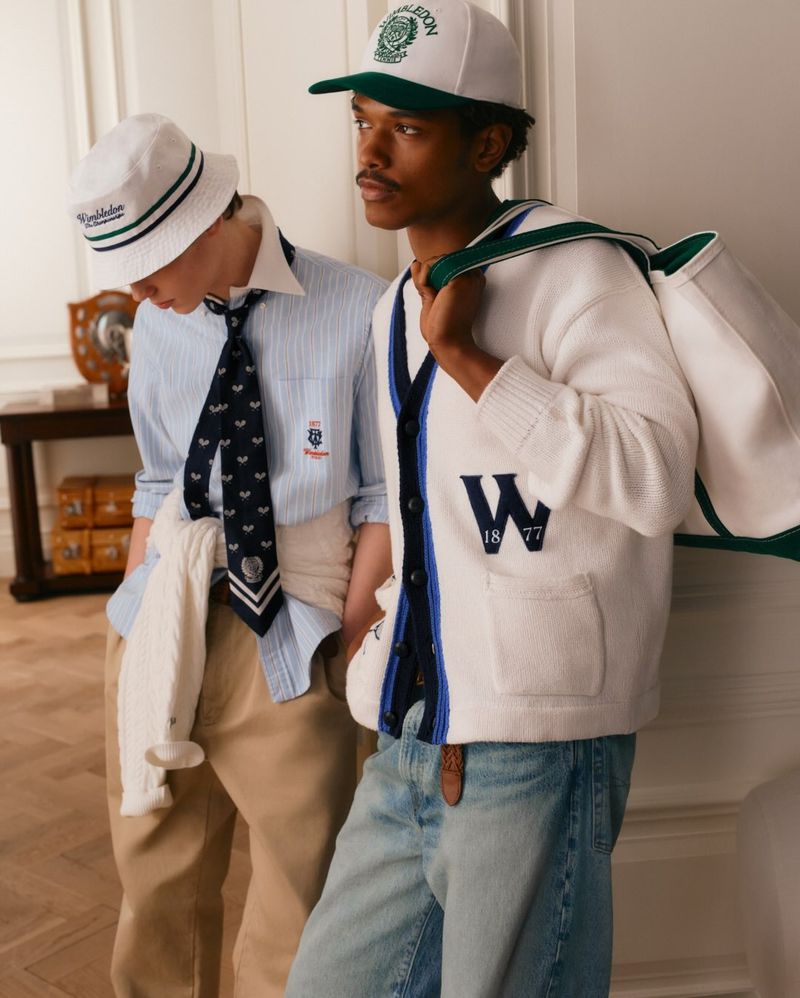 Two male models in Polo Ralph Lauren tennis apparel standing indoors near a wooden table and white wall