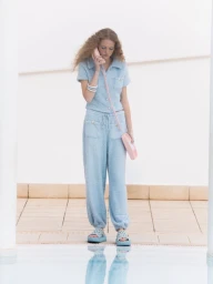 Woman in a light blue textured short-sleeve lounge set and platform slides standing poolside with a vintage pink phone.