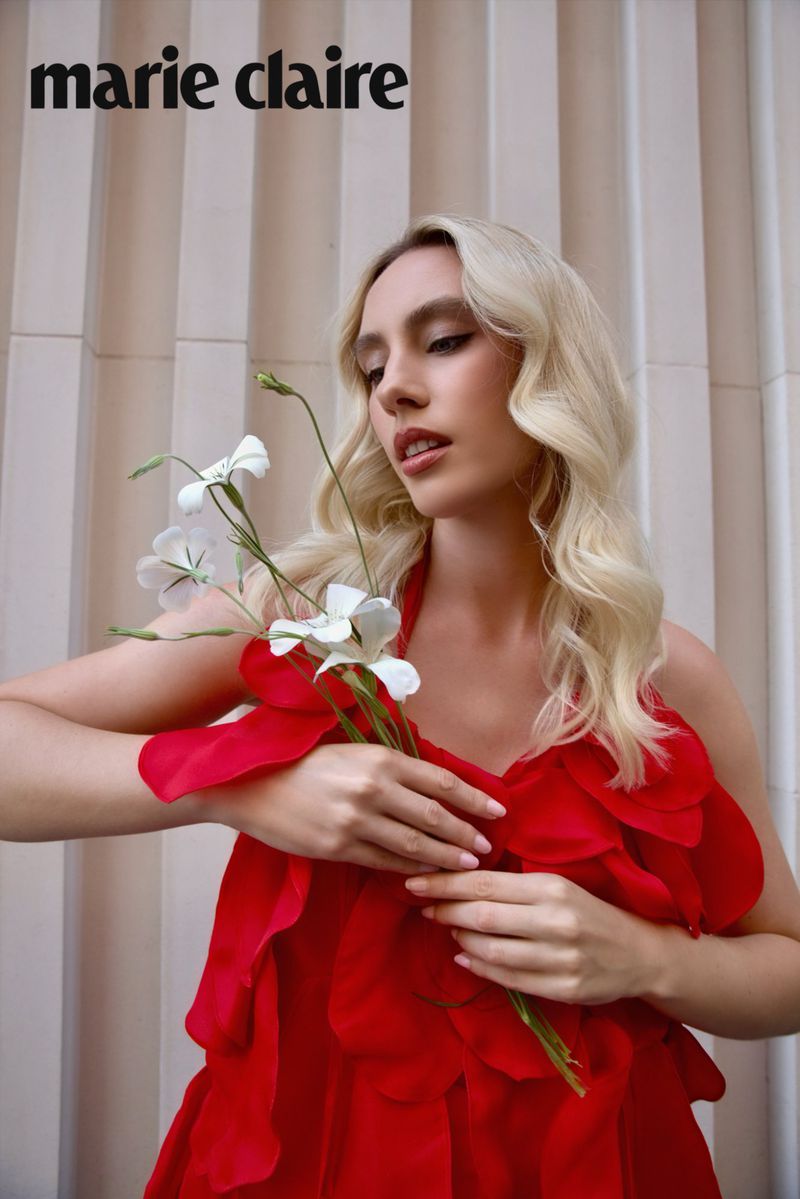 Blonde woman in a ruffled red dress holding white flowers against a fluted wall for Marie Claire Serbia.