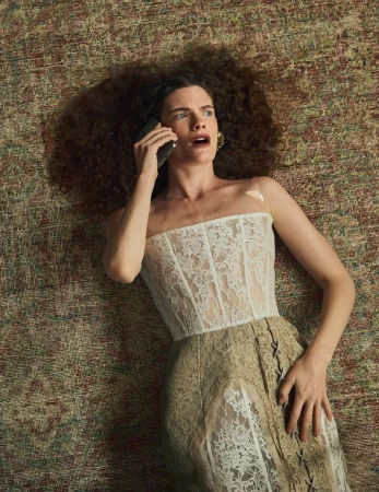 Model Carolina Burgin lying on a patterned rug in a white lace corset dress while holding a mobile phone to her ear.