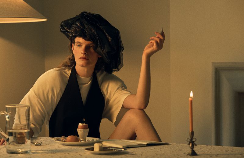 Model seated at a candlelit table wearing a black headpiece and vest over a white top for Vogue Scandinavia