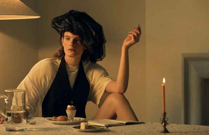 Model seated at a candlelit table wearing a black headpiece and vest over a white top for Vogue Scandinavia