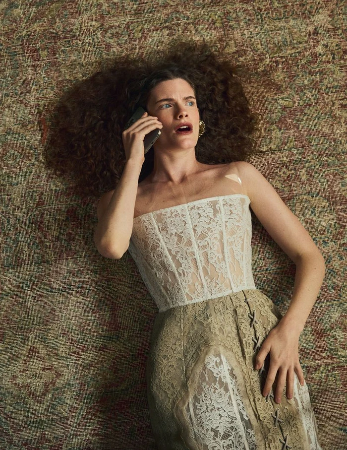 Model Carolina Burgin lying on a patterned rug in a white lace corset dress while holding a mobile phone to her ear.