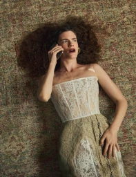 Model Carolina Burgin lying on a patterned rug in a white lace corset dress while holding a mobile phone to her ear.