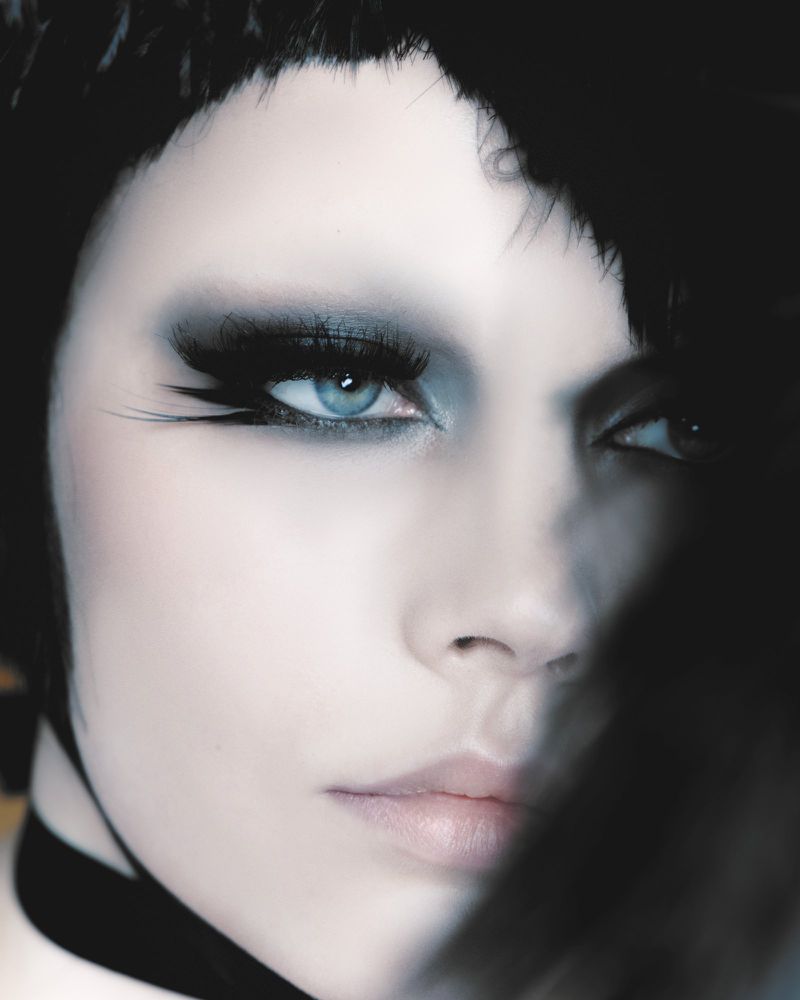 Close-up portrait of a woman with heavy smoky eye makeup, dramatic winged eyelashes, and short dark hair.
