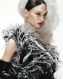 Astrid Baauer wearing an avant-garde black and white feathered garment and white mesh headdress against a white studio background.