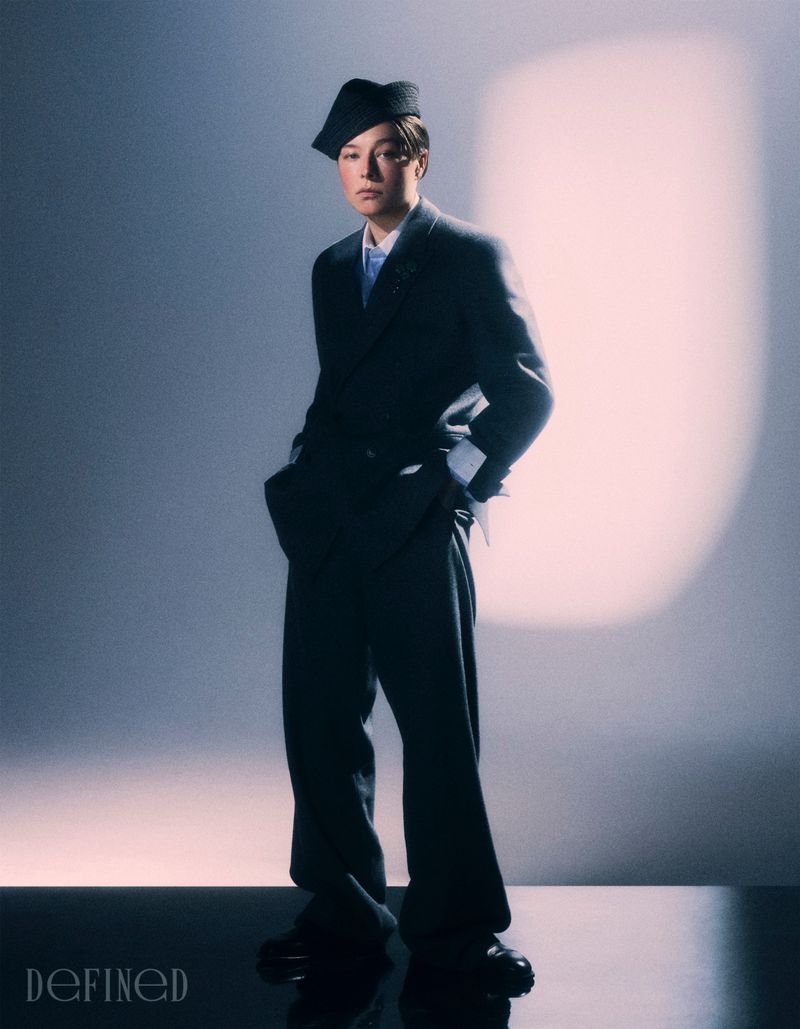 Emma D'Arcy wearing a dark suit and tilted cap in a studio portrait for DEFINED Magazine