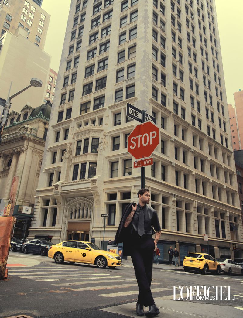 Model Emanuele Antonio Panico posing in an all-black outfit near a stop sign on an urban city street with yellow taxis.