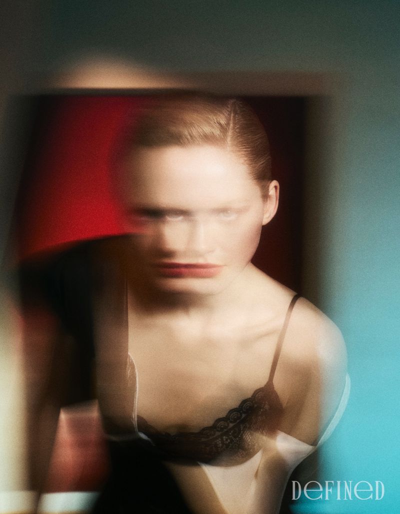 Motion-blurred portrait of Emma Laird in a black lace-trimmed camisole top against red and teal ambient lighting.