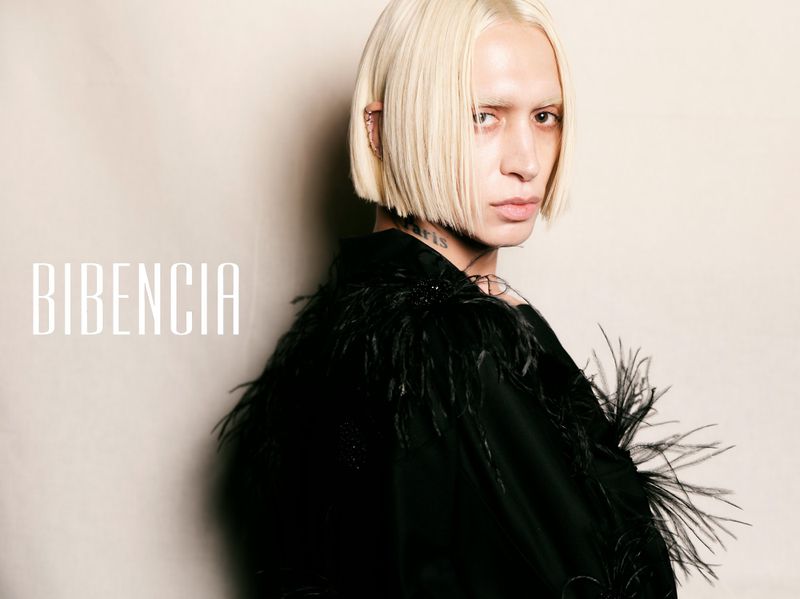 Bleached blonde model wearing a black feathered jacket against a beige background with Bibencia typography.