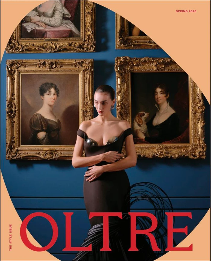 Model Neus Bermejo posing in a black off-the-shoulder gown before gold-framed oil paintings on a blue wall.