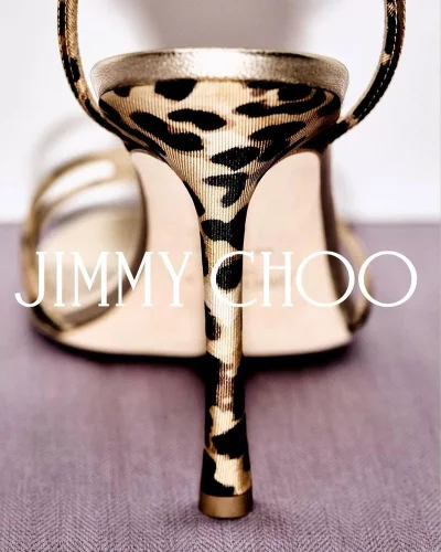 Close-up rear view of a Jimmy Choo leopard print stiletto heel sandal with gold metallic accents on a neutral surface.