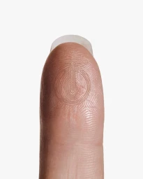 Macro view of a human fingertip with an embossed circular emblem over the fingerprint ridge patterns on a white background.
