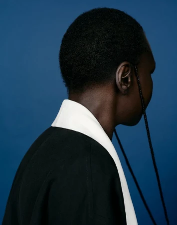 Model Alek Wek in profile wearing a black garment with white collar against a blue seamless background for CAP 74024.