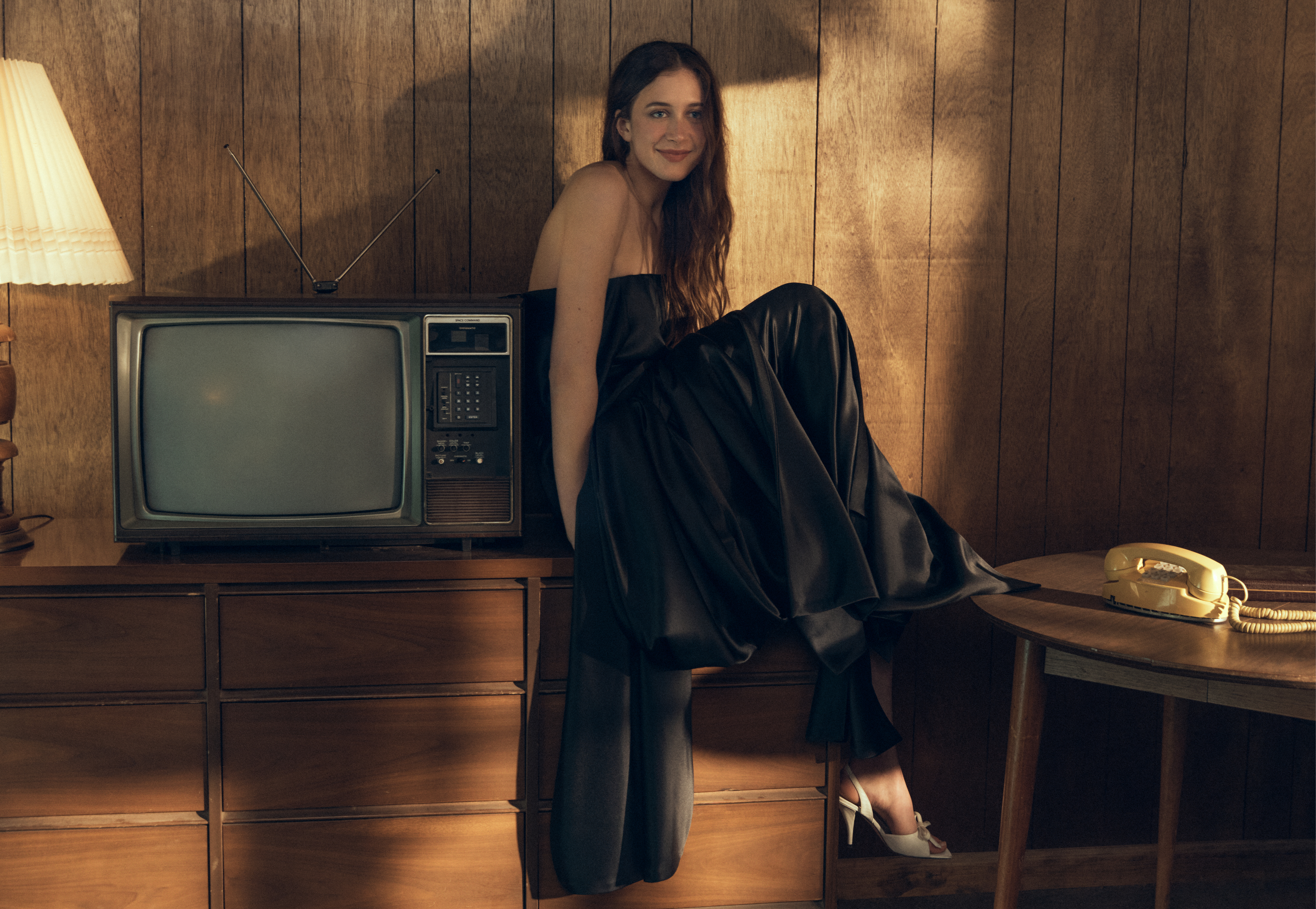 Sunday Rose Kidman Urban seated on a retro wooden credenza beside a vintage television in a black gown for Elle Australia.
