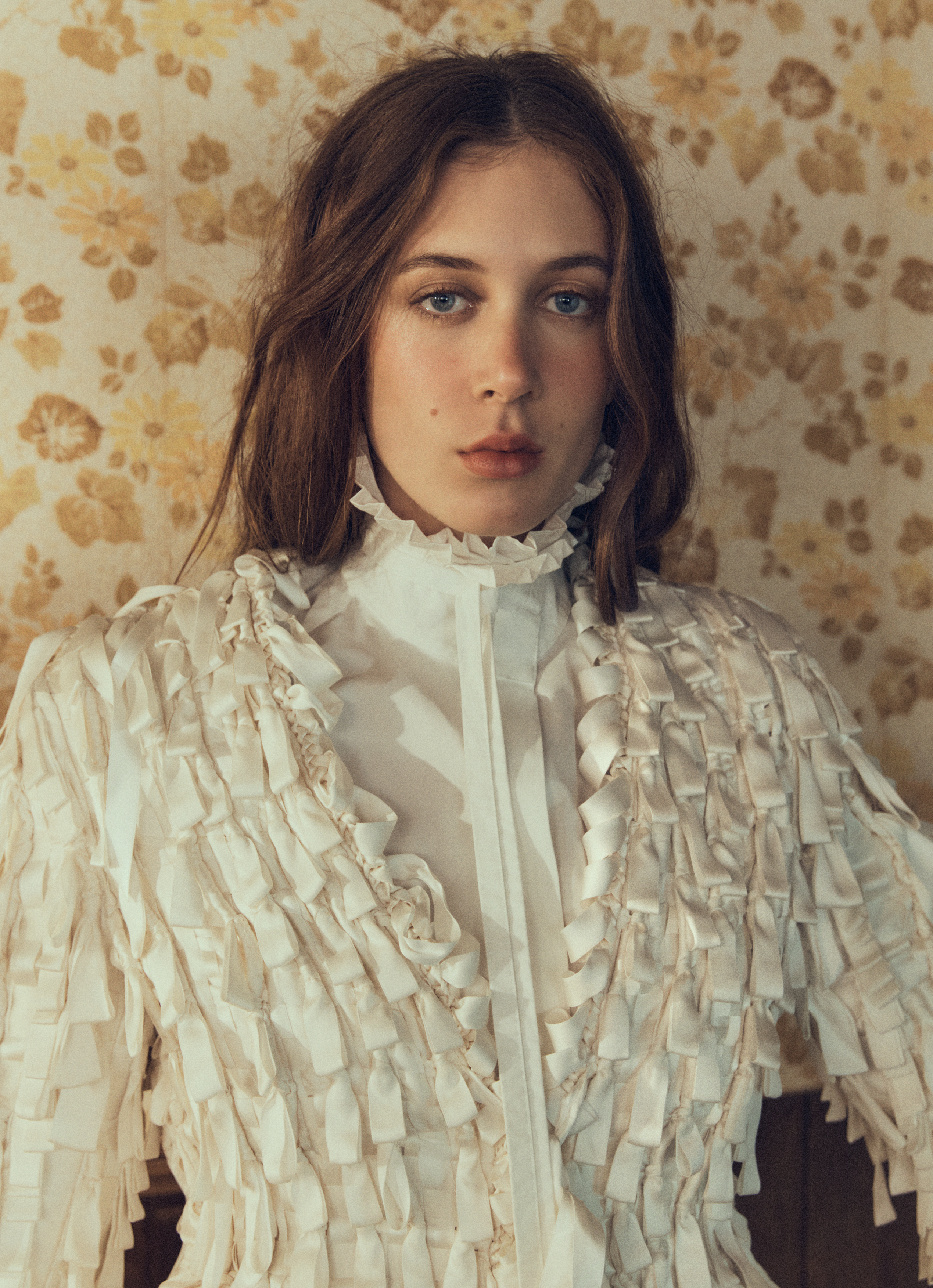 Sunday Rose Kidman Urban wearing a white textured ruffled high-collar blouse against vintage floral wallpaper.