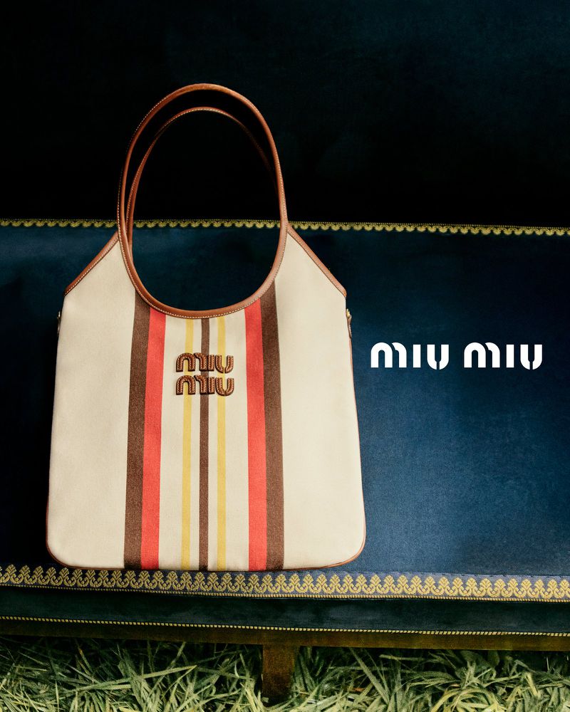 Miu Miu striped tote bag displayed on a blue velvet surface with a straw-like foreground. The bag features the brand's logo.