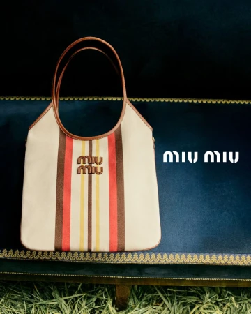 Miu Miu striped tote bag displayed on a blue velvet surface with a straw-like foreground. The bag features the brand's logo.