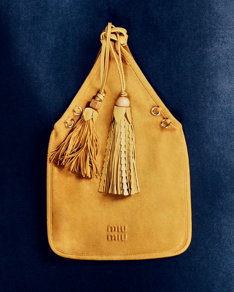 Yellow leather Miu Miu hobo bag with tassel details against a dark blue velvet background, showcasing luxury fashion and design.