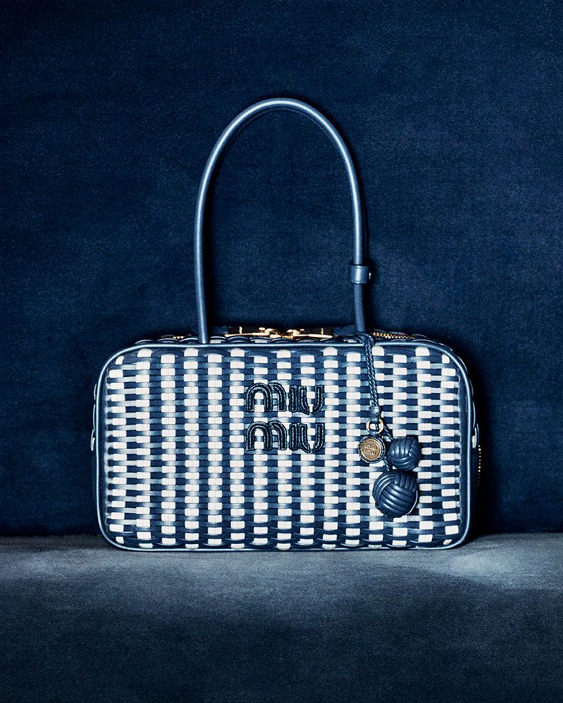 Miu Miu handbag with woven blue and white pattern, top handle, and logo charm displayed on a dark blue textured surface.
