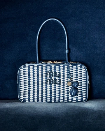 Miu Miu handbag with woven blue and white pattern, top handle, and logo charm displayed on a dark blue textured surface.