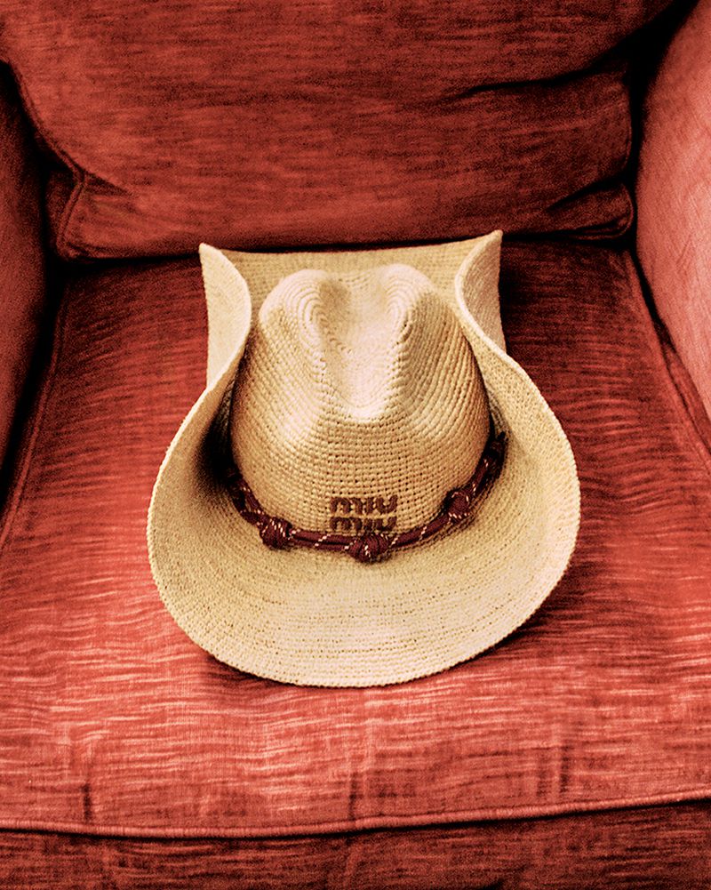Cowboy hat with Miu Miu logo sits on a plush, red chair in a close-up shot, showcasing fashion and style.