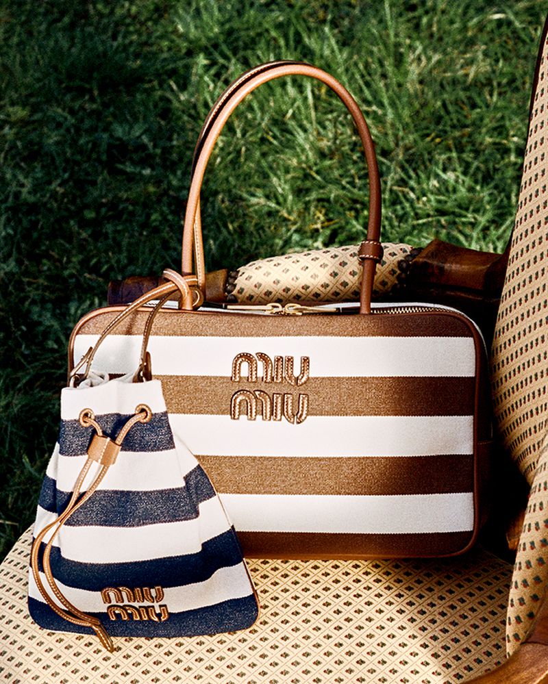 Miu Miu brown and white striped handbag and blue and white striped bucket bag on a patterned surface with a grassy background.