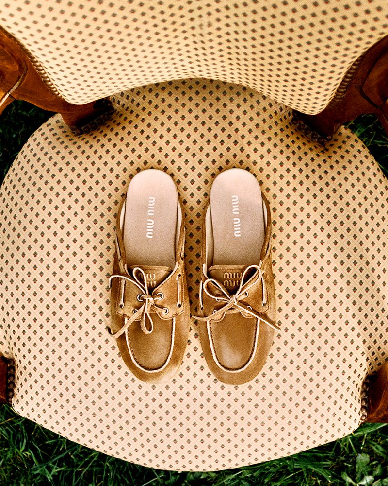 Overhead shot of Miu Miu clogs with tan uppers and cream trim sitting on a cream chair with brown patterned fabric.