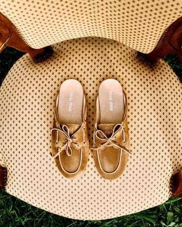 Overhead shot of Miu Miu clogs with tan uppers and cream trim sitting on a cream chair with brown patterned fabric.