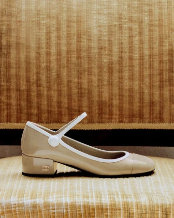 Beige patent leather Miu Miu Mary Jane low heel with white trim and button strap resting on a striped velvet chair.