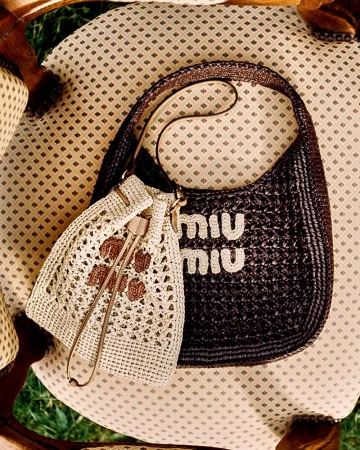 Miu Miu dark brown crochet shoulder bag and cream drawstring pouch displayed on a patterned vintage armchair.