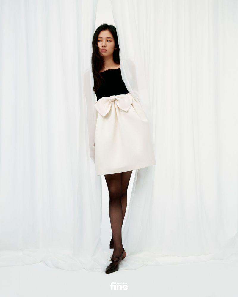 Full-length portrait of a young Asian woman in a black and white dress with a large bow, set against a pristine white fabric backdrop.