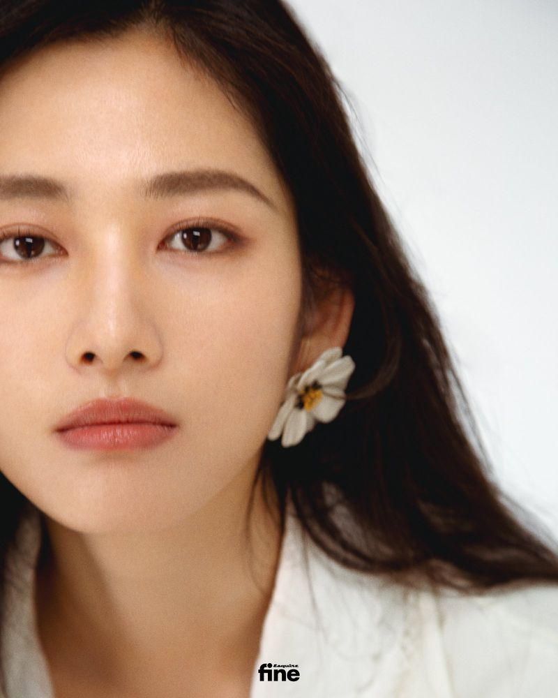 Close-up shot of an Asian woman with dark hair wearing a white jacket and a white flower earring on a white background.