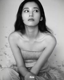 Black and white portrait of an East Asian woman wearing a strapless ribbed top, seated and looking off-camera against a studio backdrop.