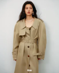 Woman wearing a beige belted trench coat and pearl necklace against a light grey background for Esquire China