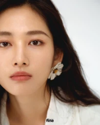 Close-up portrait of an East Asian woman wearing a white floral earring and white shirt against a plain background.