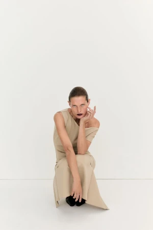 Model Malgosia Bela wearing a beige dress squatting against a plain white studio background for House of Dagmar