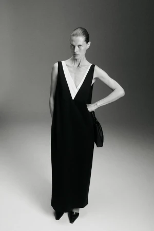 Model Malgosia Bela poses in a black sleeveless maxi dress with a deep white V-neck insert against a studio background.