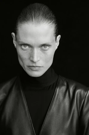 Monochrome portrait of model Malgosia Bela wearing a black turtleneck and leather V-neck garment against a black background.