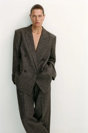 Model Malgosia Bela poses in a dark textured oversized double-breasted suit against a plain white studio background.